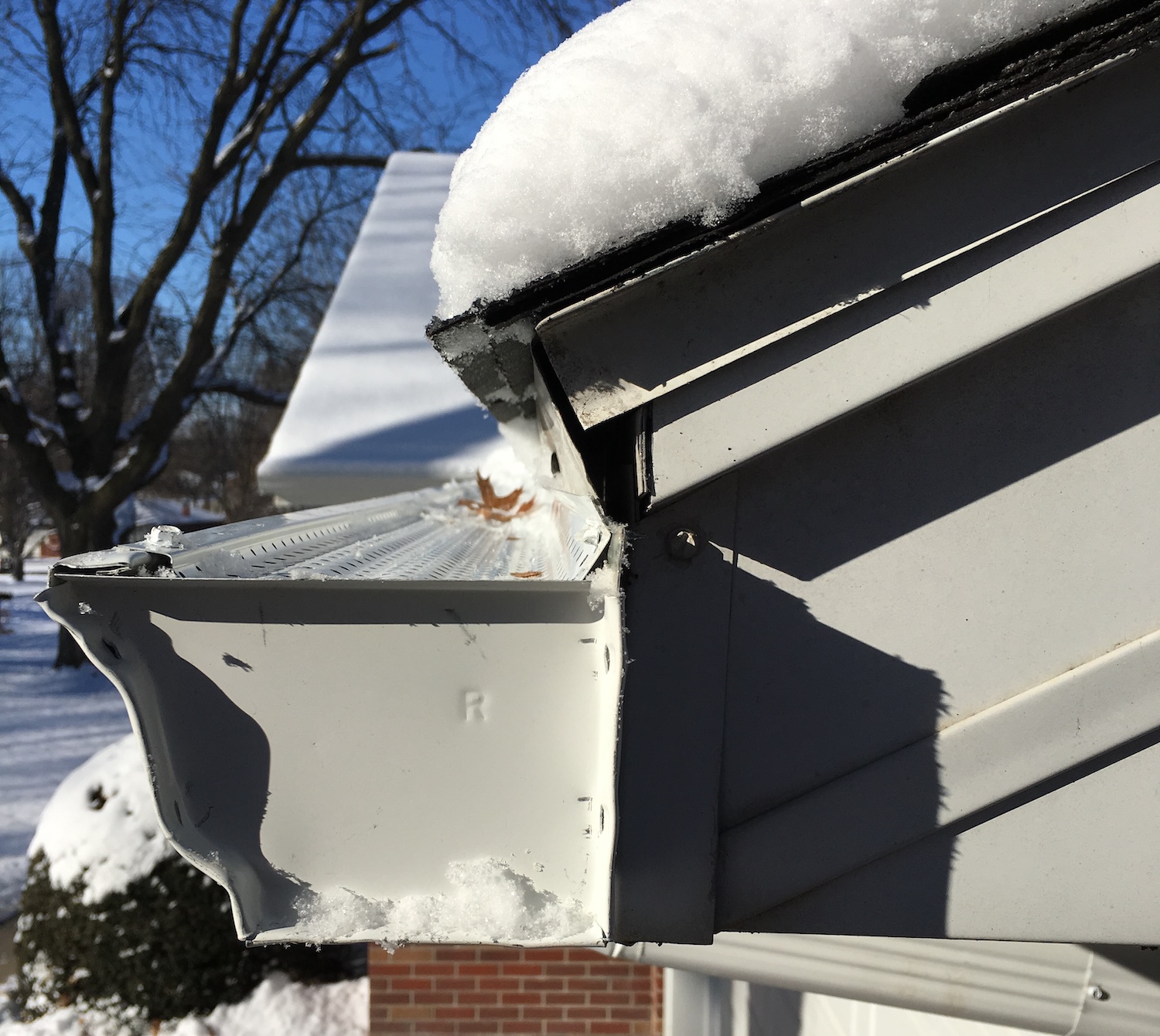 Close-up of a damaged aluminum gutter with a Gutter RX gutter guards and snow accumulation on the roof above.
