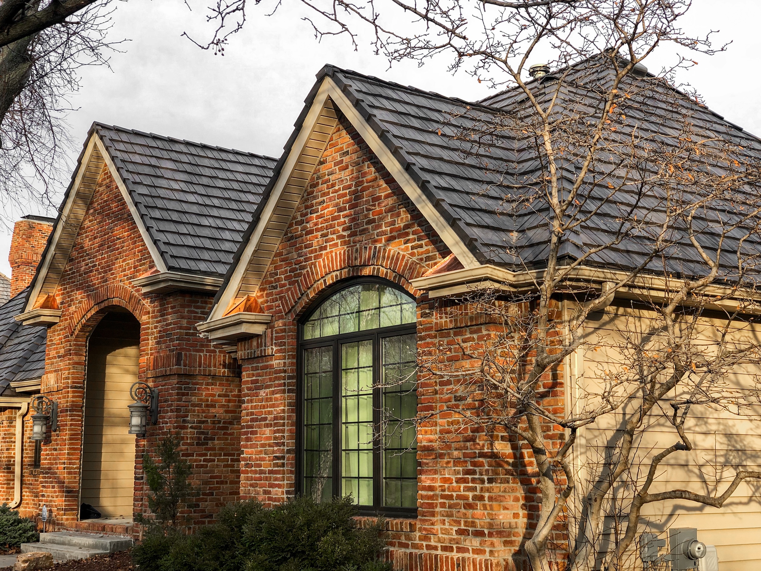 Roof Rite installed a DaVinci Single Width Shake roof on this brick and siding home, featuring a natural slate color and copper flashing accents under steep gables.